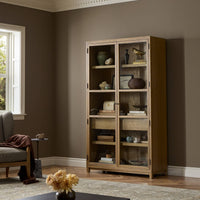 Kyra Cabinet in drifted oak with glass shelves showcasing decorative items.