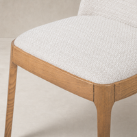 Rhys Armless Dining Chair featuring Gibson Wheat upholstery and natural wood legs.