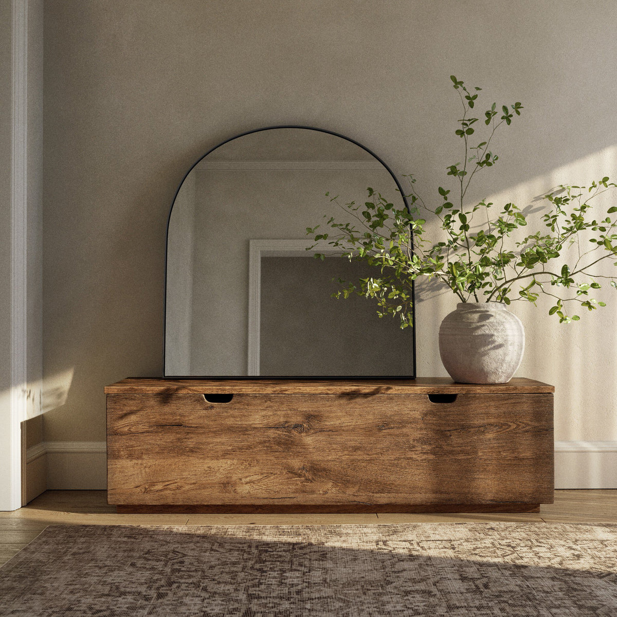 Elena Wide Mirror in iron matte black above a modern wooden dresser with greenery.