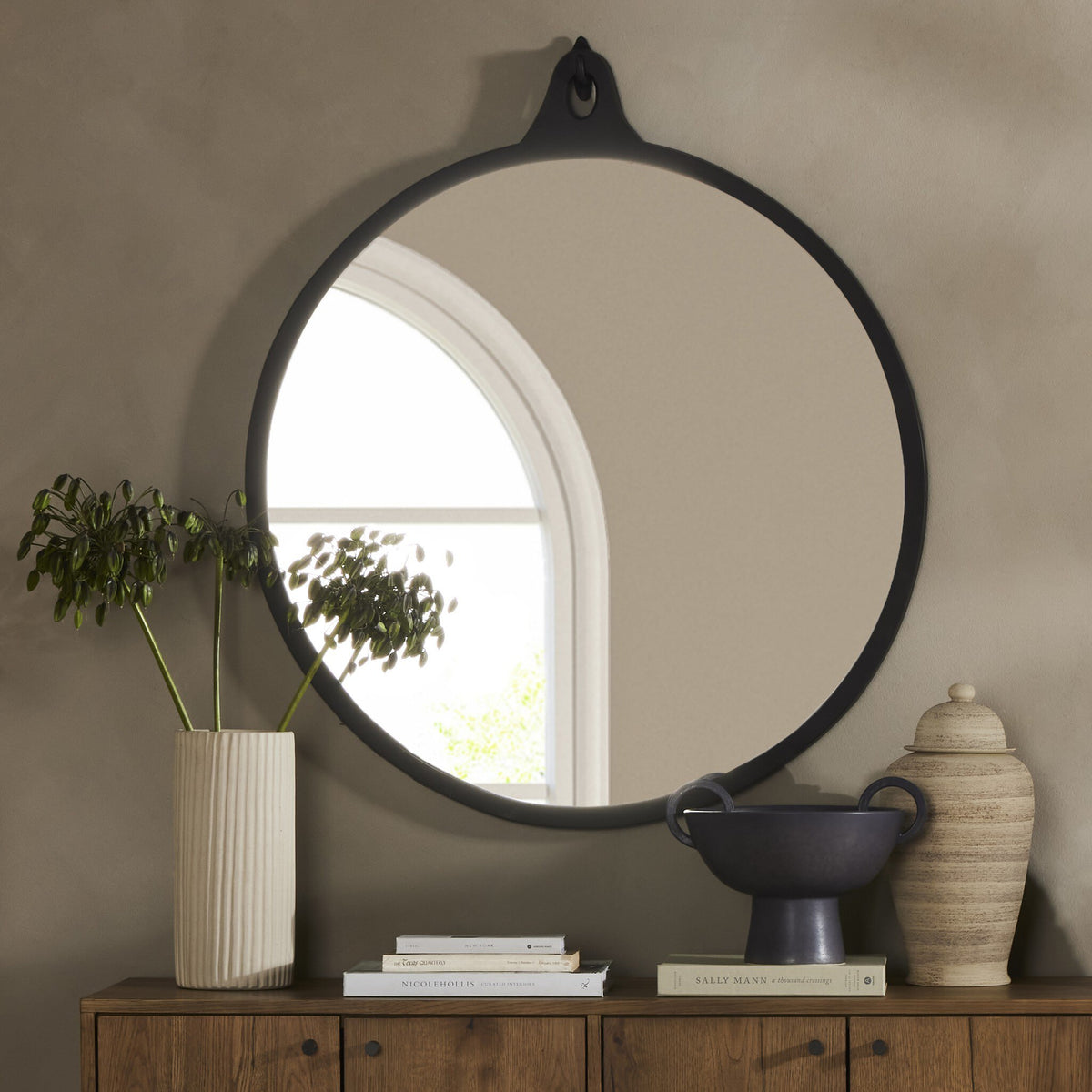 Knox Round Mirror in black aluminum, reflecting a cozy room setting with plants.