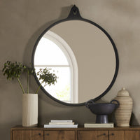 Knox Round Mirror in black aluminum, reflecting a cozy room setting with plants.