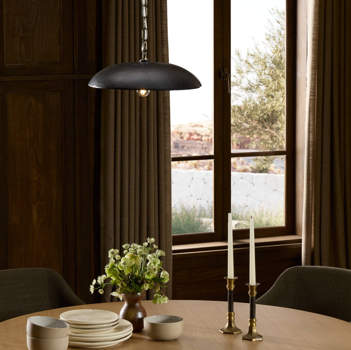 Aged black terracotta ceramic pendant light hanging above a wooden dining table.