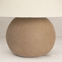 Dark sand porcelain ceramic table lamp with textured round base and fabric shade.