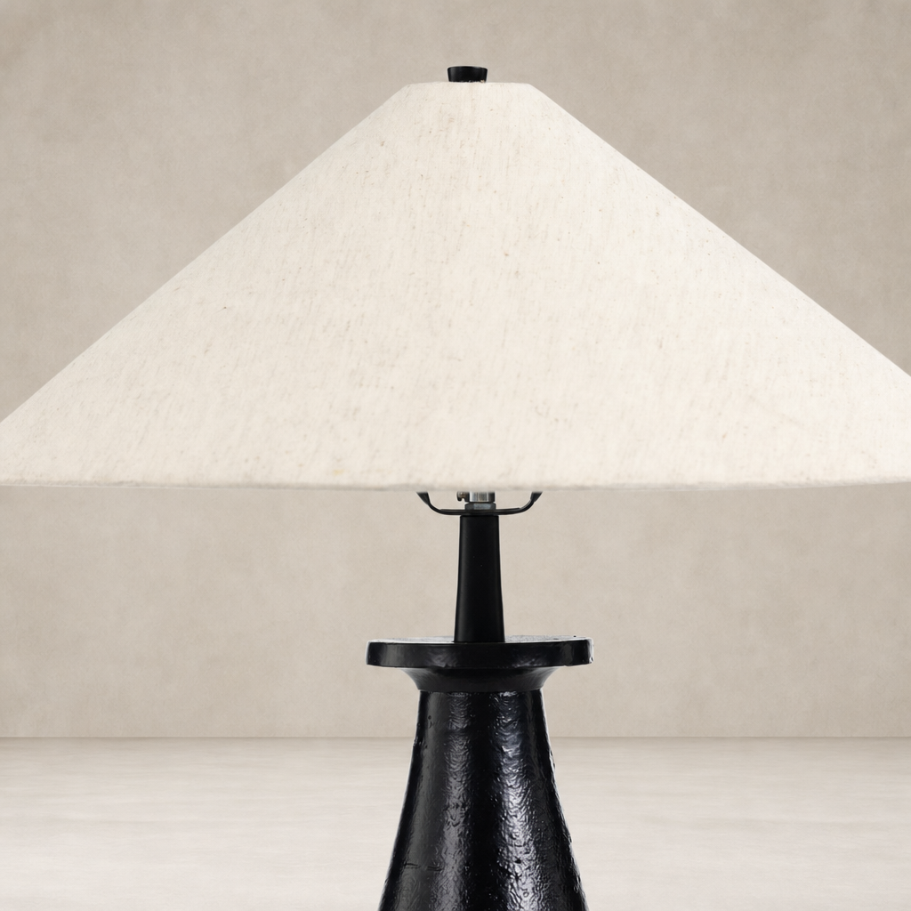 Matte black cast aluminum tapered shade table lamp with a light fabric shade.