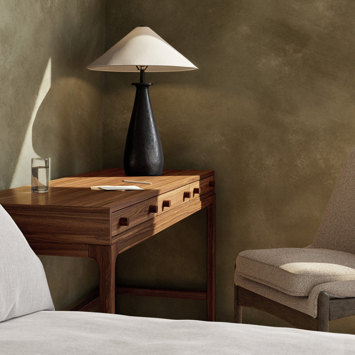 Matte black cast aluminum tapered shade table lamp on wooden bedside table.