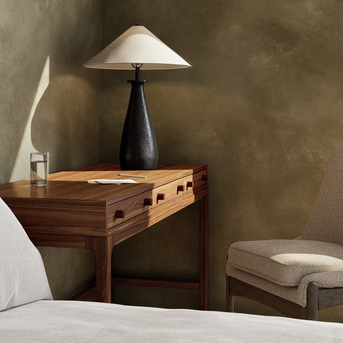 Matte black cast aluminum tapered shade table lamp on wooden bedside table.
