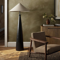 Matte black cast aluminum tapered shade floor lamp in a cozy room setting.