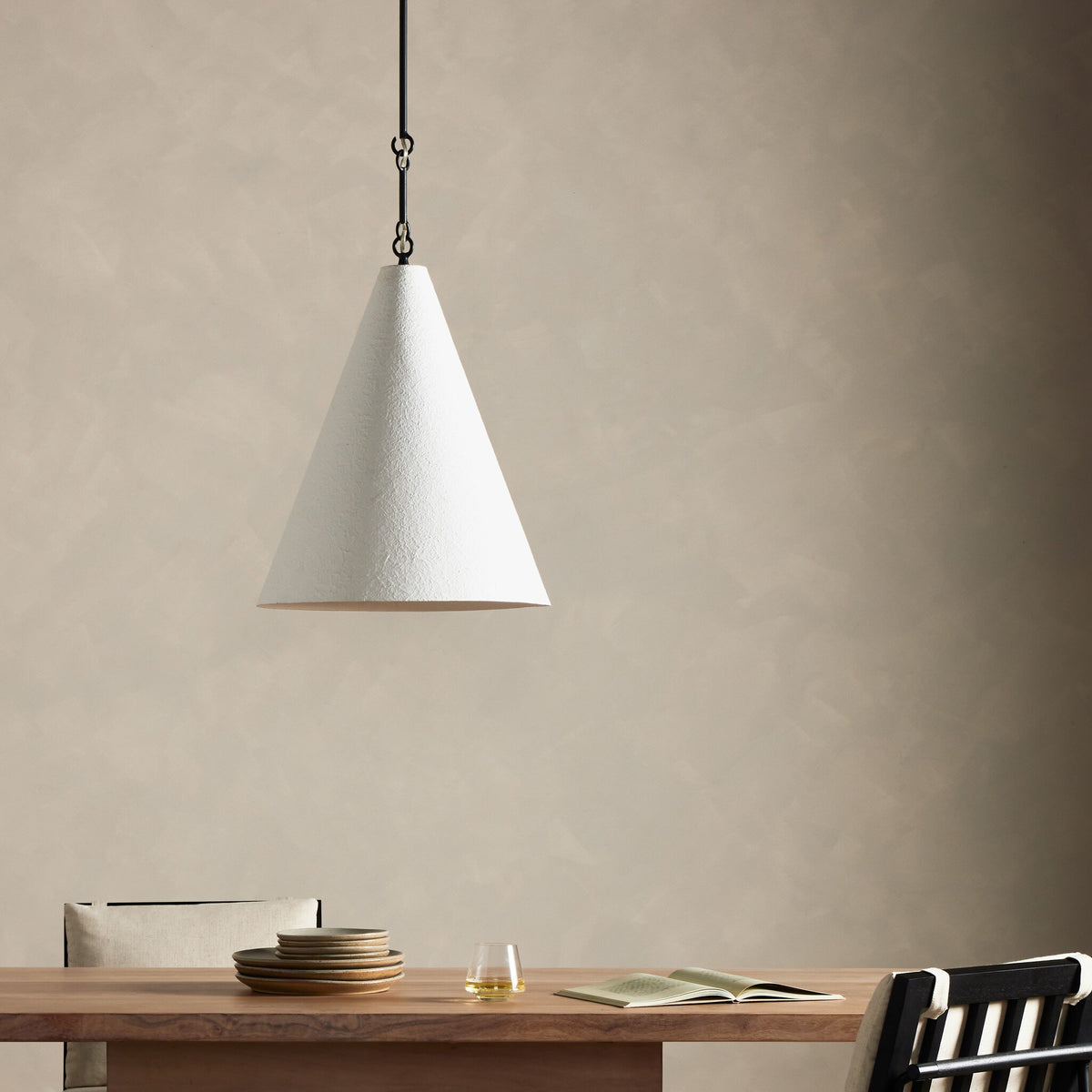 Matte white plaster pendant light hanging over a wooden dining table.