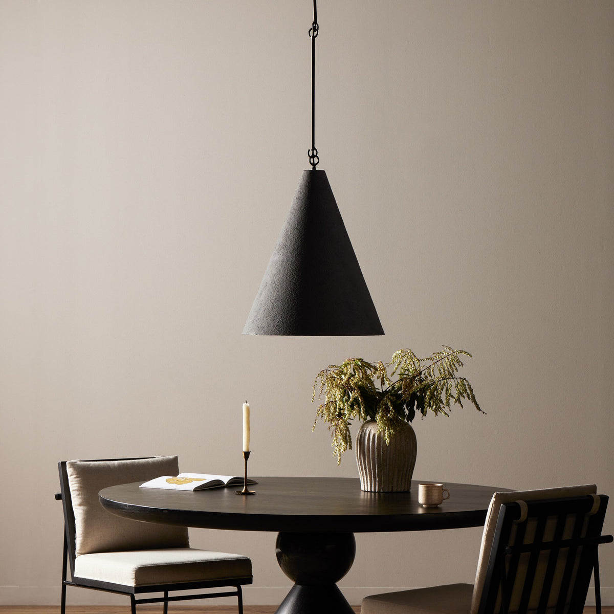 Matte black plaster pendant light hanging over a round dining table setting.