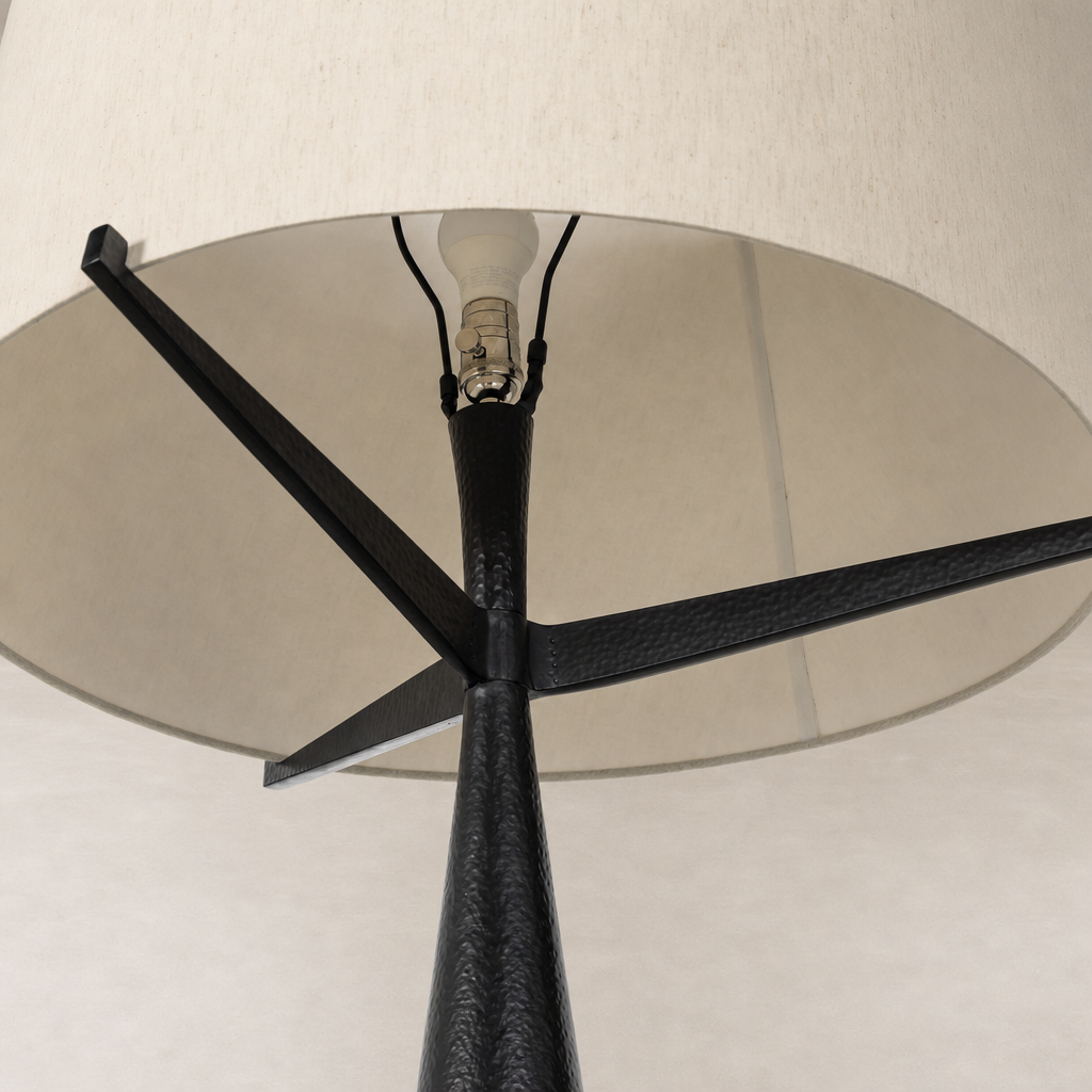 Hammered black aluminum floor lamp with a neutral fabric shade and elegant tripod design.