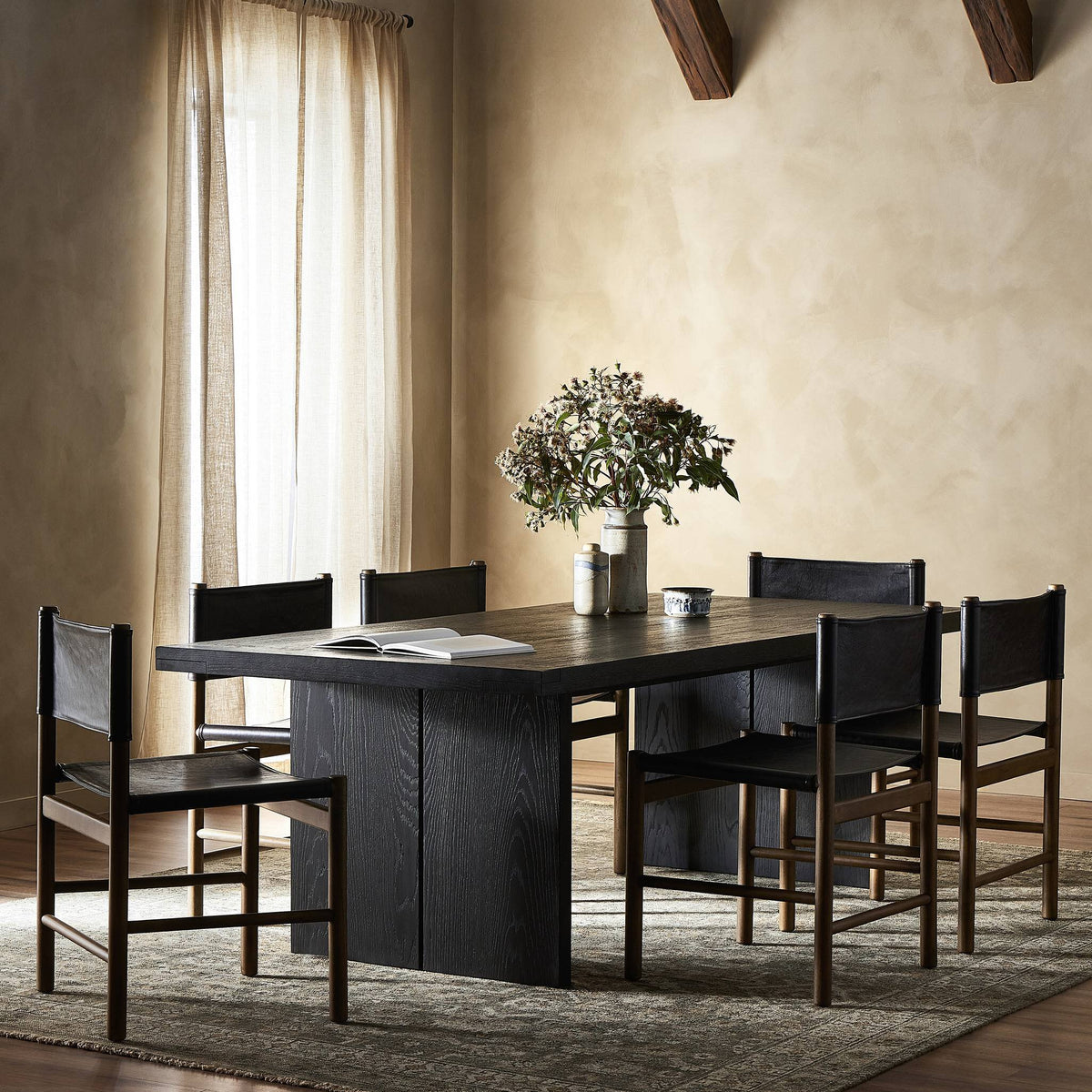 Sevilla Dining Table in worn black oak with minimalist design and matching chairs.