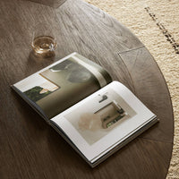 Hastings Coffee Table in warm natural flat oak with an open magazine and glass.