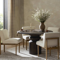 Three-quarter view of the Ravello Round Dining Table, featuring a dark wood finish and a sculptural base, surrounded