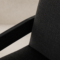Close-up of a Gibson Black dining armchair featuring textured fabric and sleek wooden armrests.