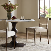 Mira Armless Dining Chair in Antwerp Natural, featuring a soft fabric seat and sleek wood legs.