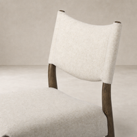 Mira Armless Dining Chair in Antwerp Natural featuring a soft, textured fabric and wooden legs.
