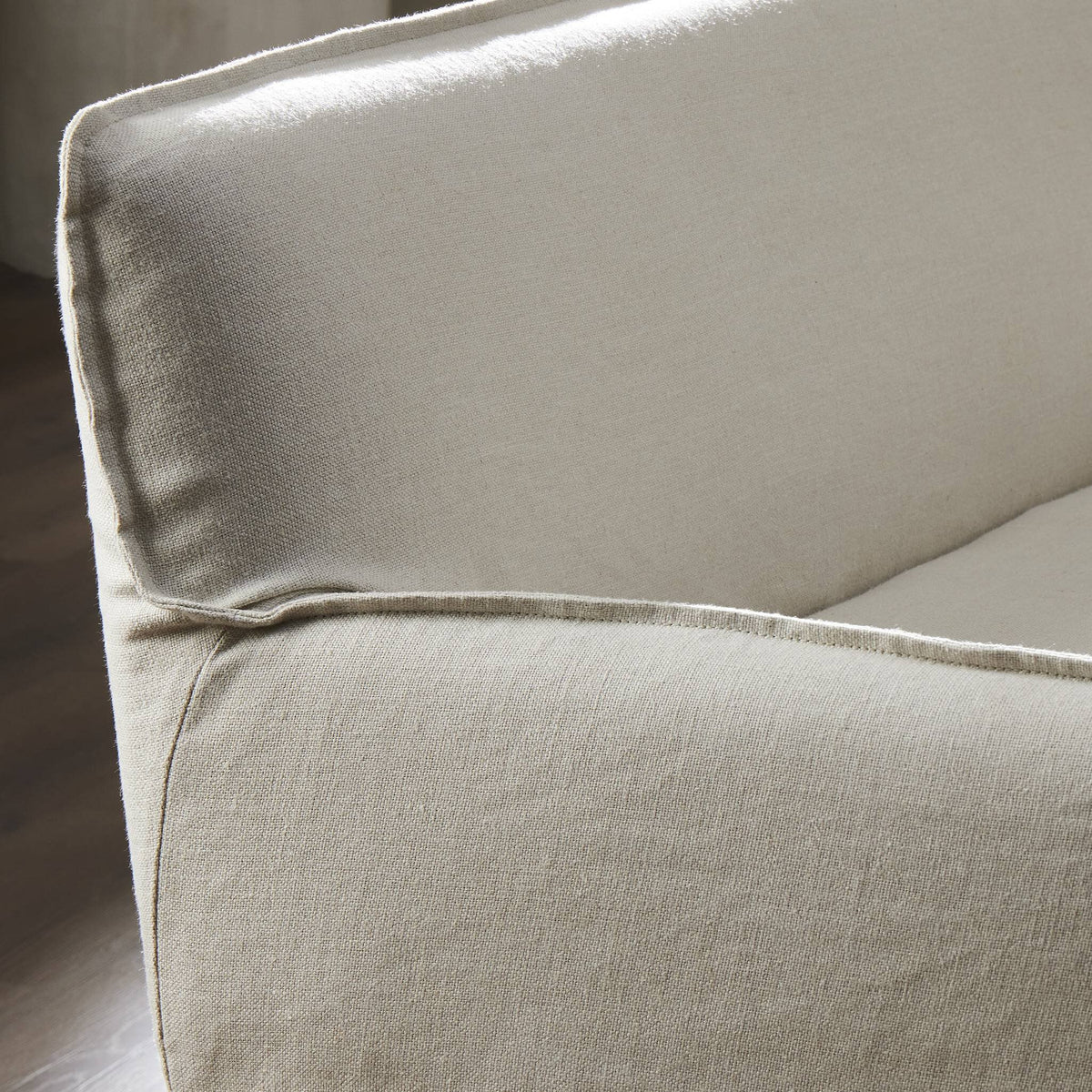 Slipcovered upholstered bench in cream fabric with a low back and wood legs.