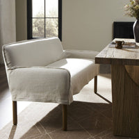 Slipcovered upholstered dining bench in cream fabric with a low back and wood legs in dining room