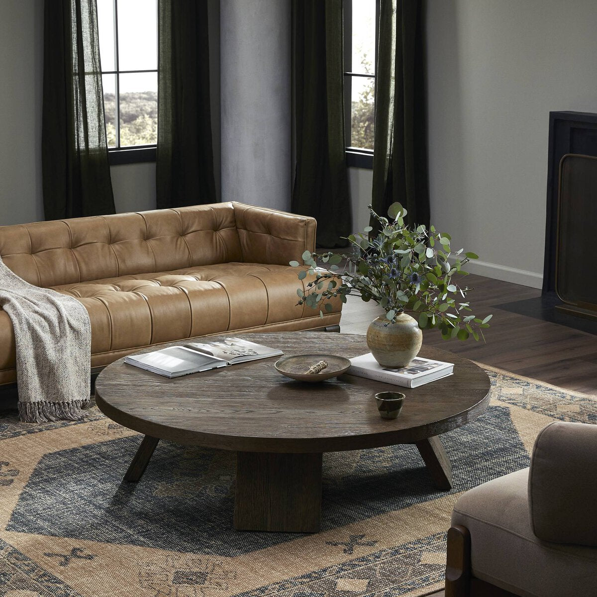 Three-quarter view of the Juniper Coffee Table in a cozy living room, showcasing its round shape and rustic finish.