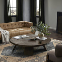 Three-quarter view of the Juniper Coffee Table in a cozy living room, showcasing its round shape and rustic finish.