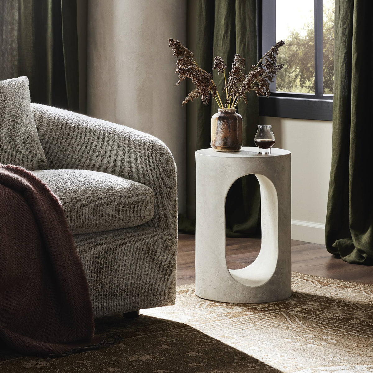 Atlas End Table with a circular design and open cutout, set beside a cozy sofa.