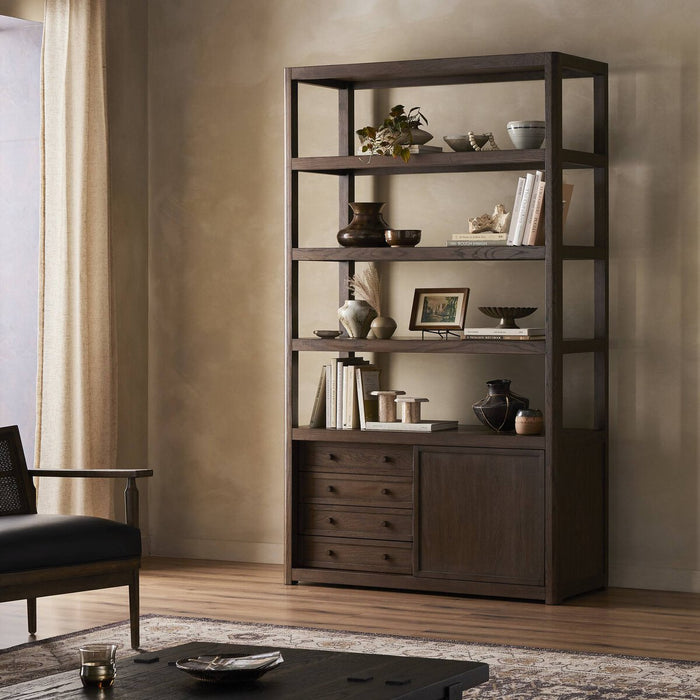 Three-quarter view of the Greer Bookcase in a warm wood finish, featuring open shelving and closed storage.