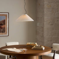 Jet black pendant light with pleated design hanging above a wooden table.