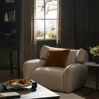 Allora Swivel Chair in Saxon Sand with plush cushion in a cozy living room setting.