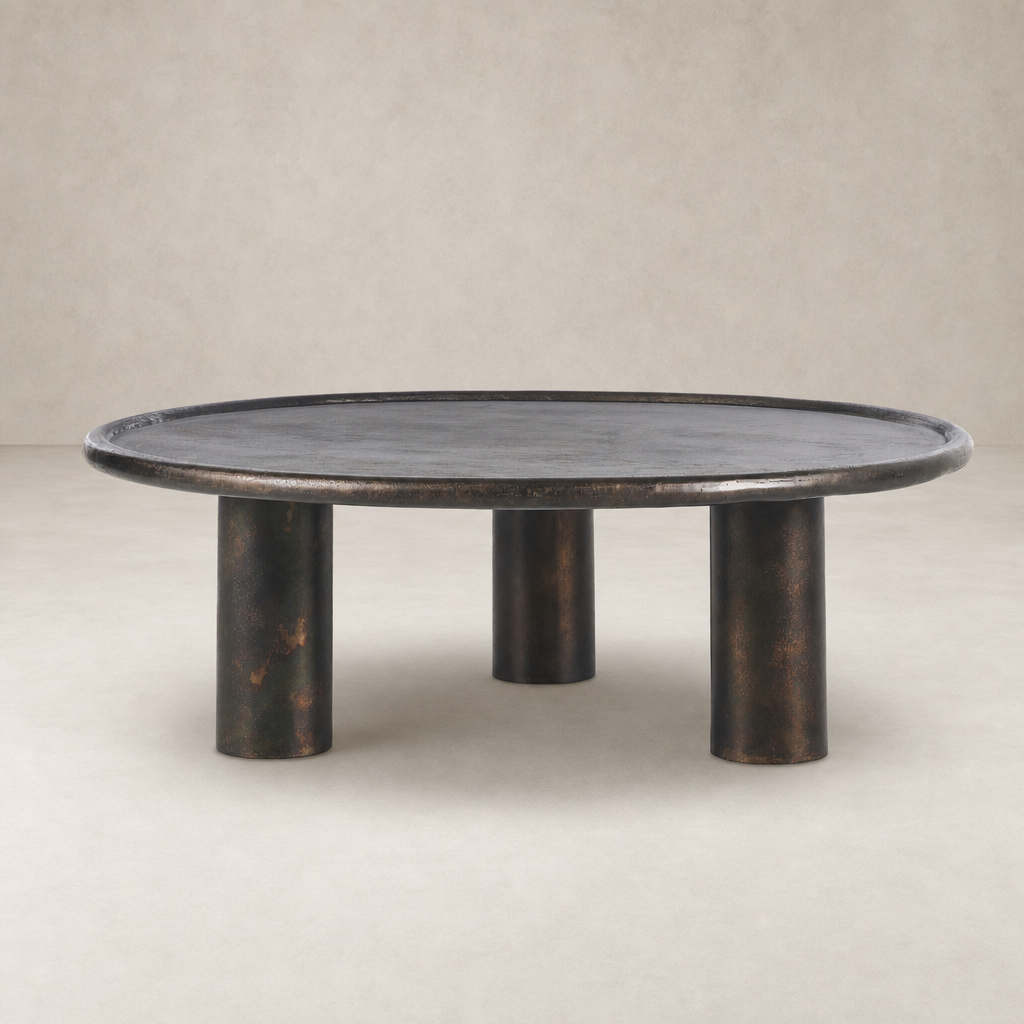 Cade Coffee Table with distressed bronze finish and rounded design on three cylindrical legs.
