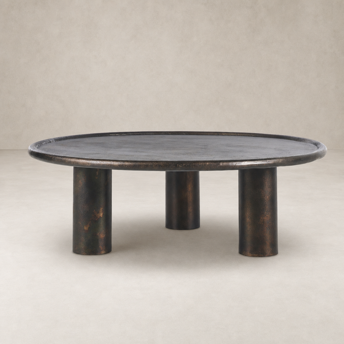 Cade Coffee Table with distressed bronze finish and rounded design on three cylindrical legs.