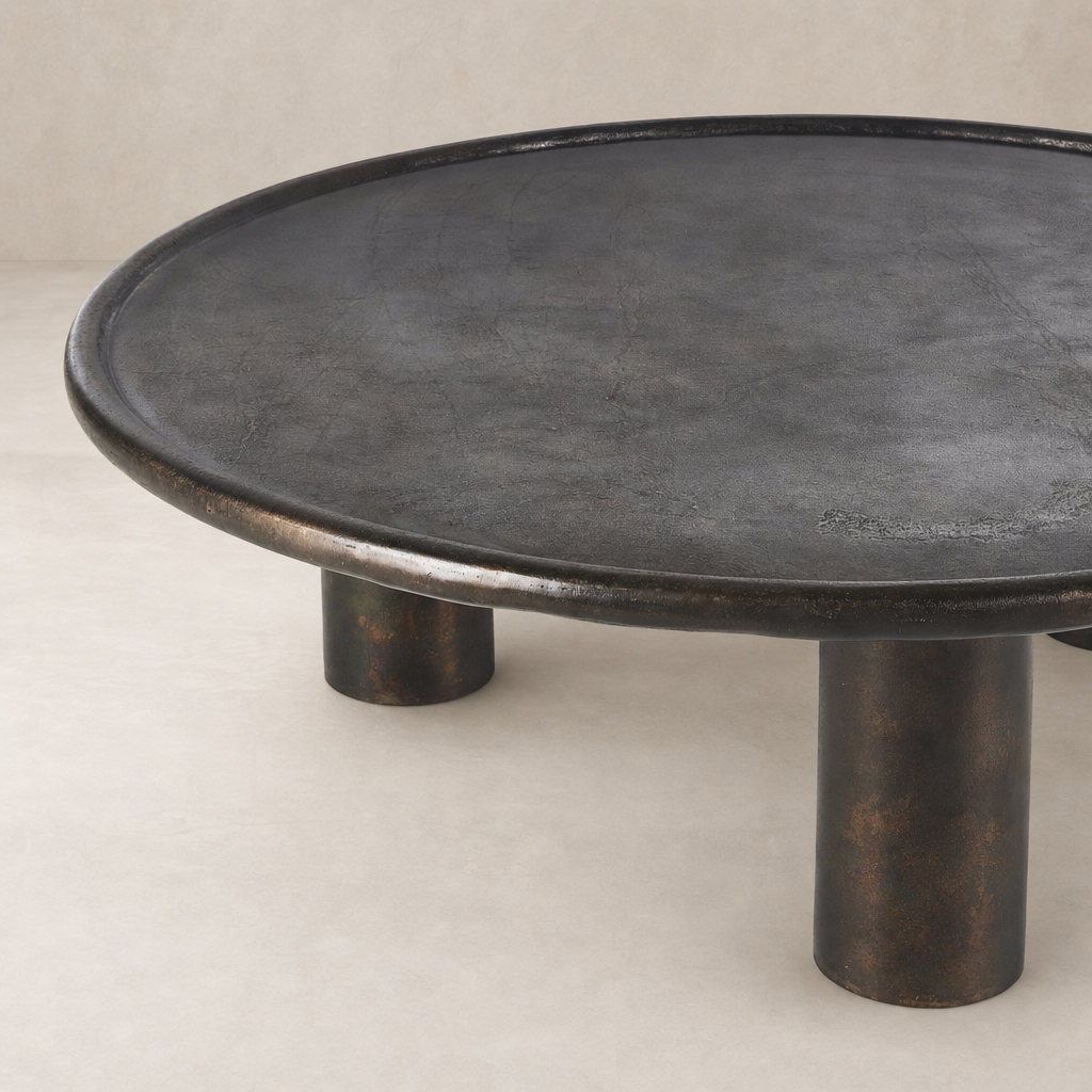 Cade Coffee Table in distressed bronze with a round top and bold pedestal legs.