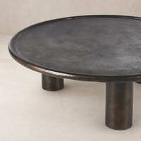Cade Coffee Table in distressed bronze with a round top and bold pedestal legs.