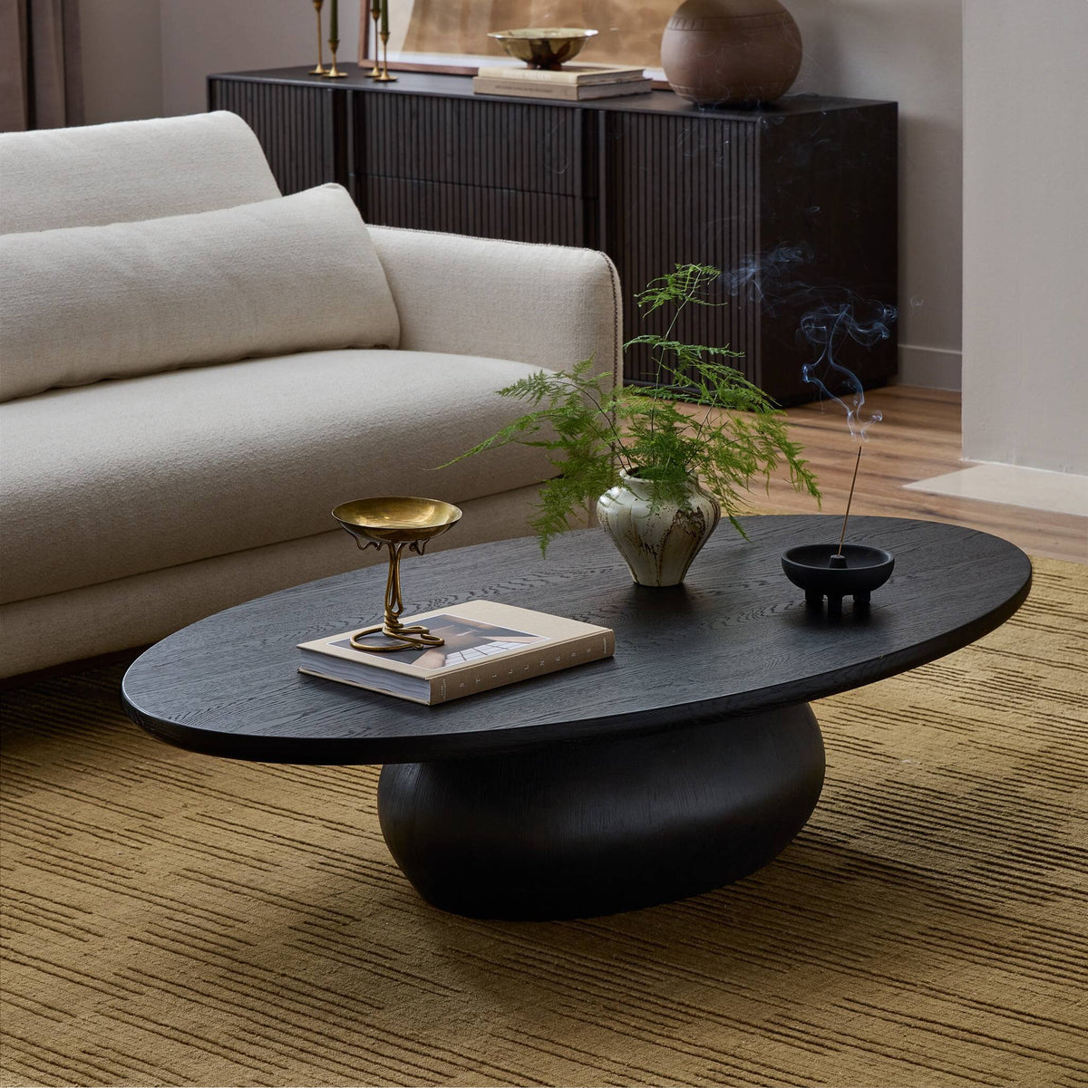 Ronan Coffee Table in worn black with an oval top and sculptural base, styled in a cozy living room.
