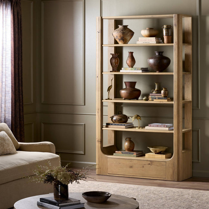 Orion Bookcase in aged natural oak showcasing decorative pottery and books in a cozy living space.
