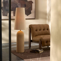 Tan speckled ceramic floor lamp with a tapered shade in a cozy living room setting.