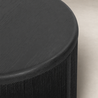 Roselle End Table features a sleek, round black wood surface with ribbed detailing.