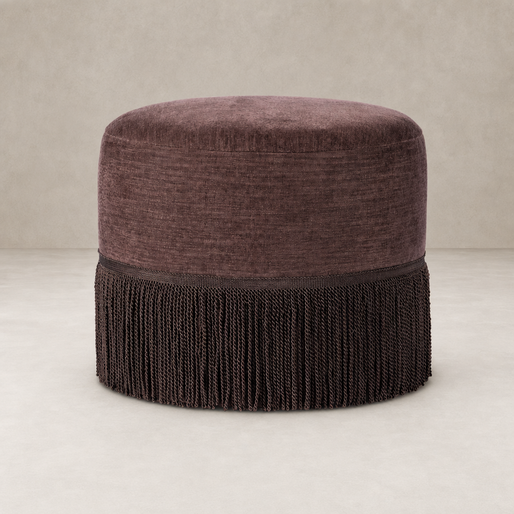 Round Laughlin Plum fringe ottoman with textured upholstery and decorative tassels.