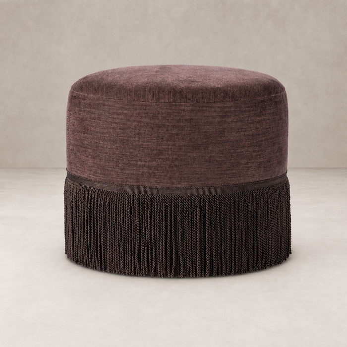 Round Laughlin Plum fringe ottoman with textured upholstery and decorative tassels.