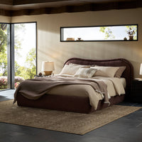Plum upholstered bed with curved headboard, layered bedding, and warm ambient lighting.