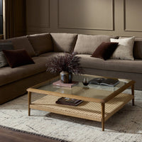 Brandy Coffee Table featuring a tempered glass top and woven rattan shelf in a cozy living room setting.