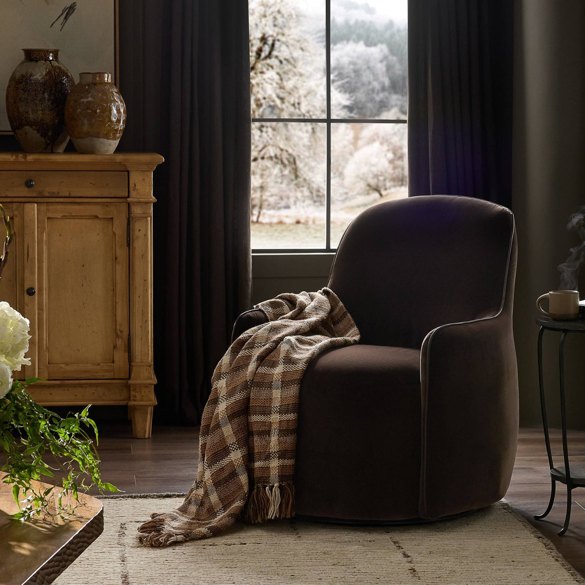 Paloma Swivel Chair in Surrey Cocoa with a cozy blanket draped over it.
