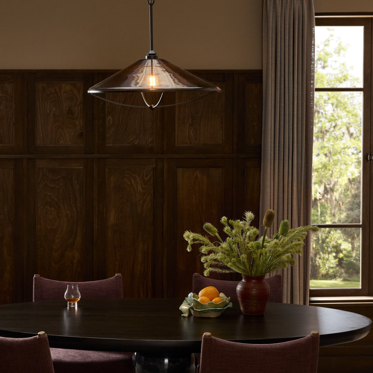 Amber glass pendant lamp with a sleek, conical shape illuminating a dining area.