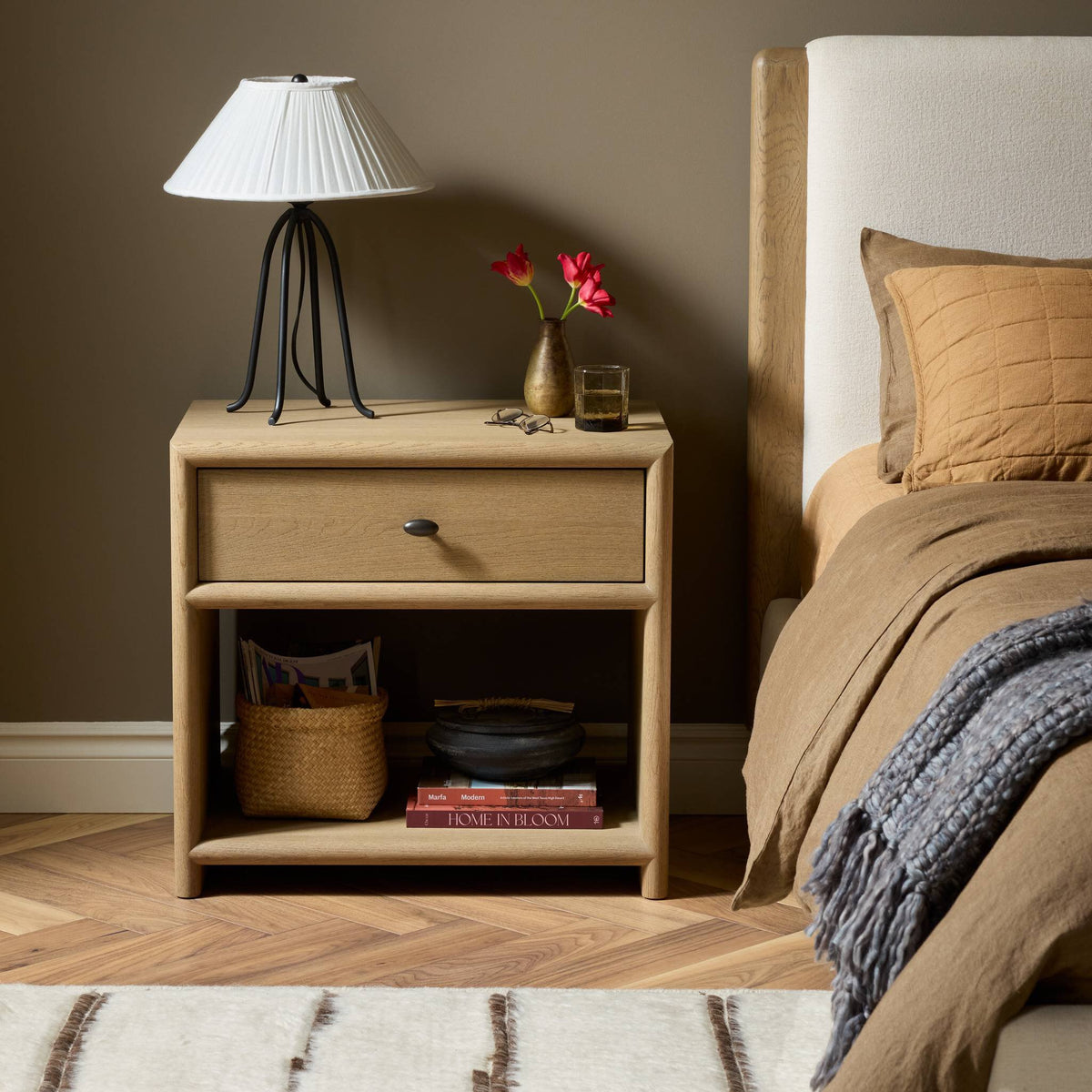 Sandy oak nightstand with a drawer and open shelf in a cozy bedroom setting.