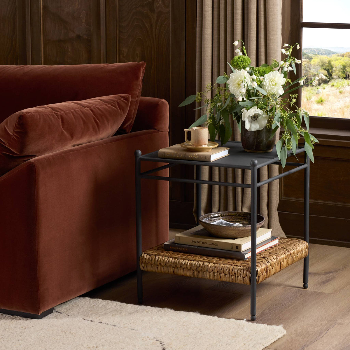 Colette End Table features a sleek black top and woven natural fiber shelf, styled with decor.