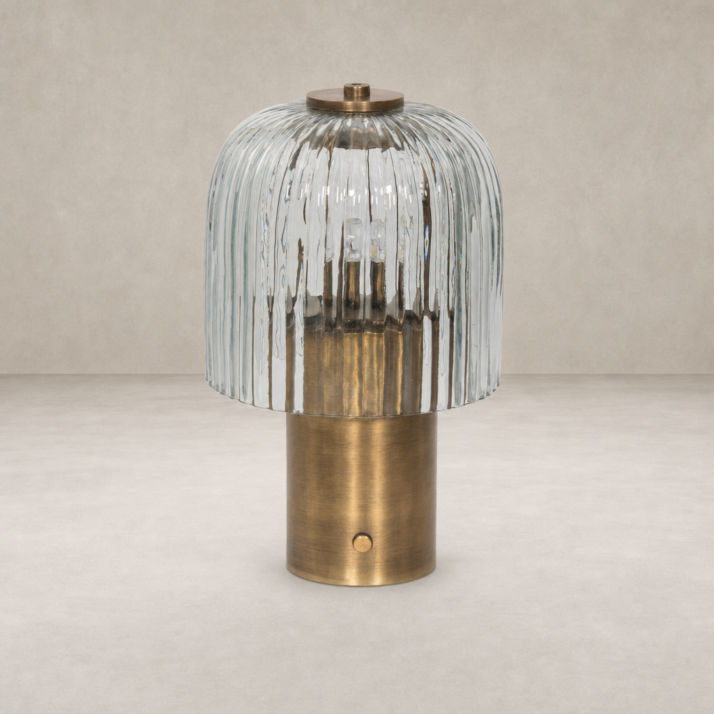 Cordless table lamp in aged antique brass iron with a textured glass shade.