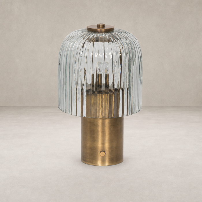 Cordless table lamp in aged antique brass iron with a textured glass shade.