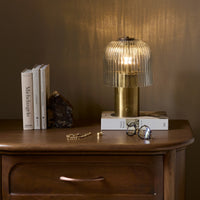 Cordless table lamp in aged antique brass iron with ribbed glass shade.