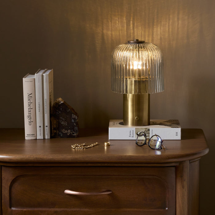 Cordless table lamp in aged antique brass iron with ribbed glass shade.