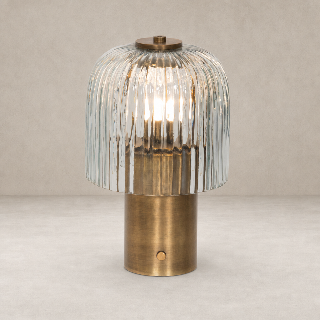 Cordless table lamp in aged antique brass iron with a fluted glass shade.