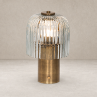 Cordless table lamp in aged antique brass iron with a fluted glass shade.